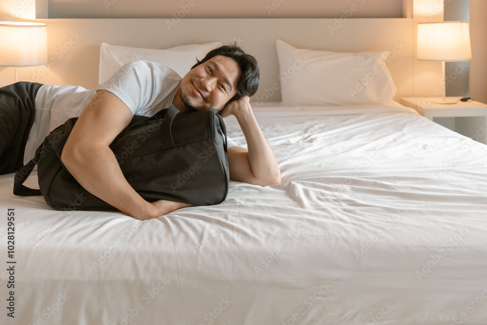 Happy Asian man lying on the hotel bed with luggage travel bag. Happy Asian man lying on the hotel bed with luggage travel bag.