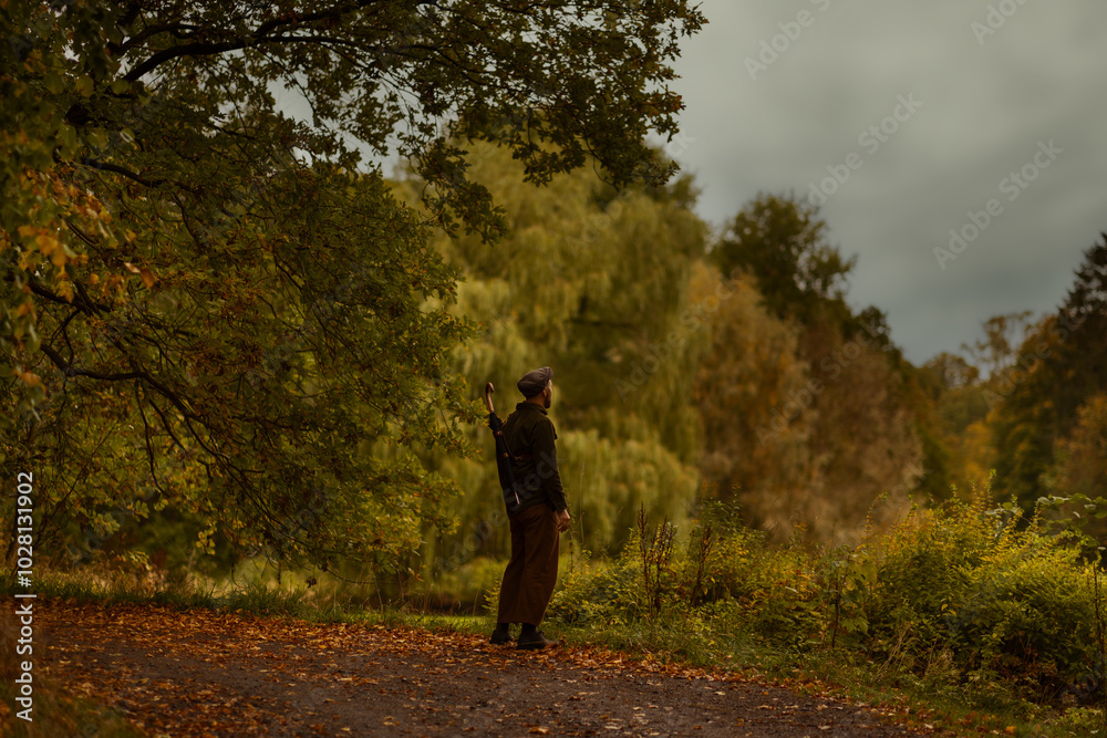 A caucasian man standing on a road watching an autumn landscape wearing autumn clothes and an umbrella sling. A caucasian man standing on a road watching an autumn landscape wearing autumn clothes and an umbrella sling.