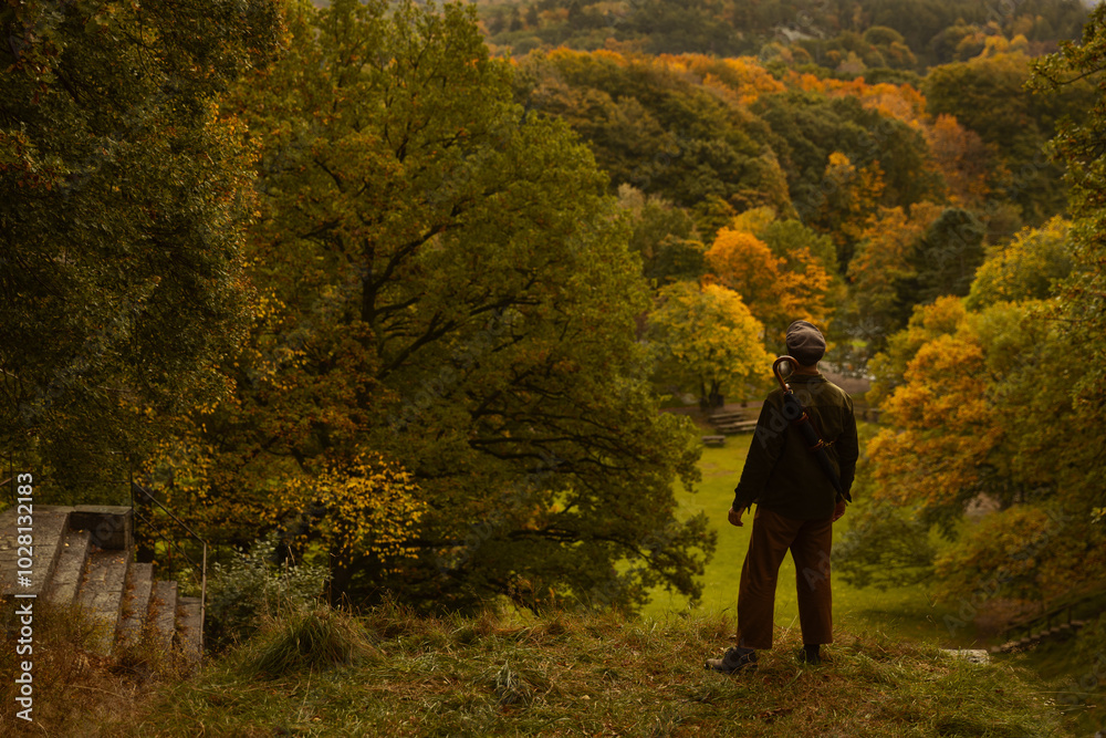 A caucasian man standing on a hill watching an autumn landscape wearing autumn clothes and an umbrella sling. A caucasian man standing on a hill watching an autumn landscape wearing autumn clothes and an umbrella sling.