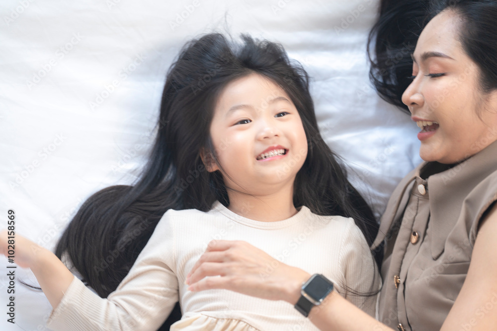 A joyful mother and daughter laughing together while lying on a bed. The playful moment showcases their strong bond and happiness in a comfortable home setting, surrounded by natural decor. A joyful mother and daughter laughing together while lying on a bed. The playful moment showcases their strong bond and happiness in a comfortable home setting, surrounded by natural decor.