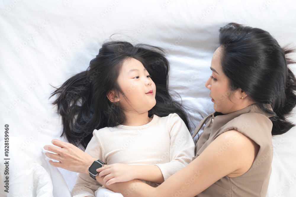 A joyful mother and daughter laughing together while lying on a bed. The playful moment showcases their strong bond and happiness in a comfortable home setting, surrounded by natural decor. A joyful mother and daughter laughing together while lying on a bed. The playful moment showcases their strong bond and happiness in a comfortable home setting, surrounded by natural decor.