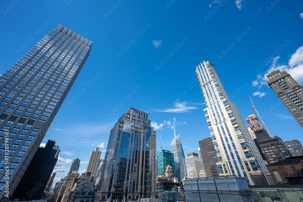 Fototapeta premium Stunning rooftop views of New York City’s skyline, featuring iconic skyscrapers under a clear blue sky. The crisp architecture contrasts against the vivid urban landscape, offering a classic perspecti