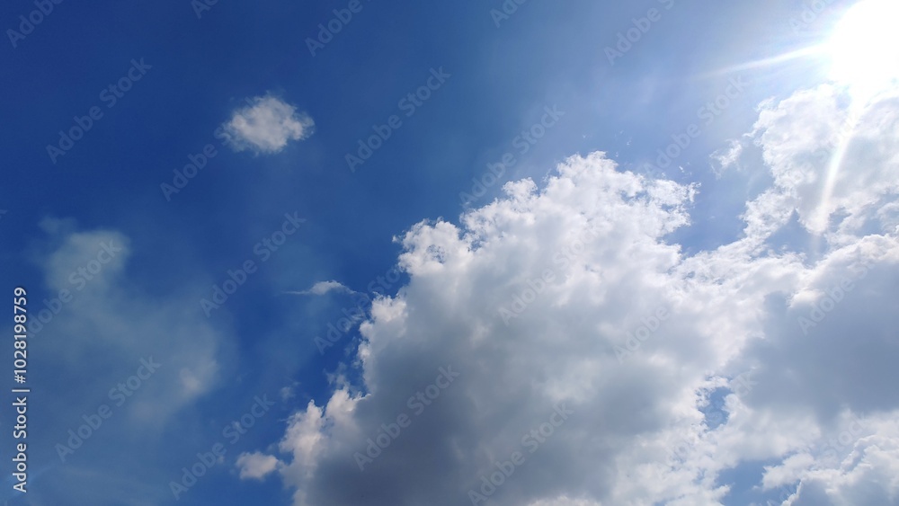 A bright blue sky with fluffy white clouds and the sun shining through. A bright blue sky with fluffy white clouds and the sun shining through.