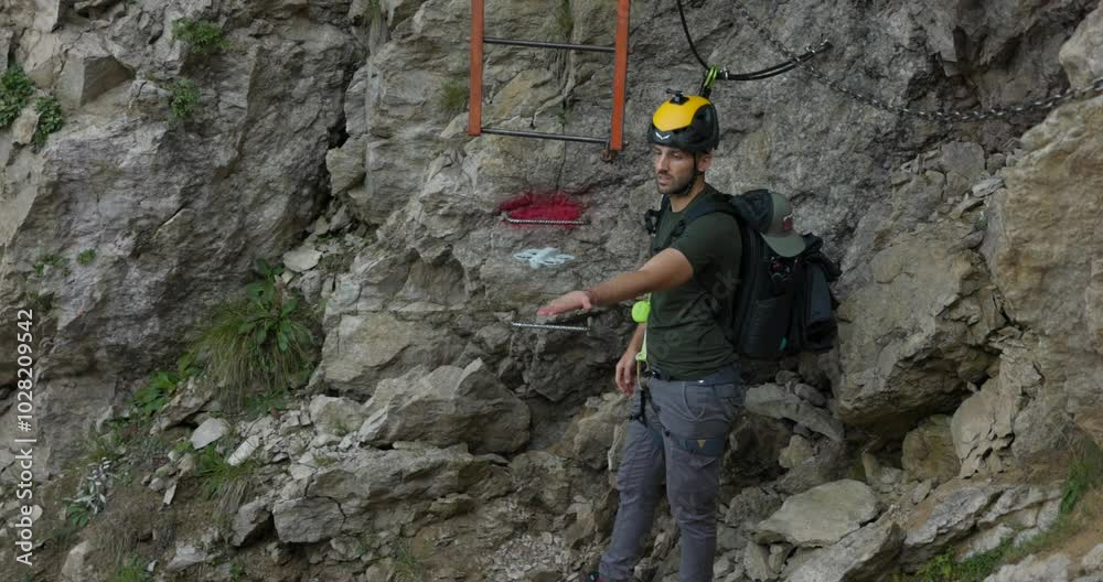 A man prepares to record himself with a drone on a rocky mountain trail, equipped with safety gear and a helmet. The scene highlights adventure, self-filming, and outdoor exploration A man prepares to record himself with a drone on a rocky mountain trail, equipped with safety gear and a helmet. The scene highlights adventure, self-filming, and outdoor exploration