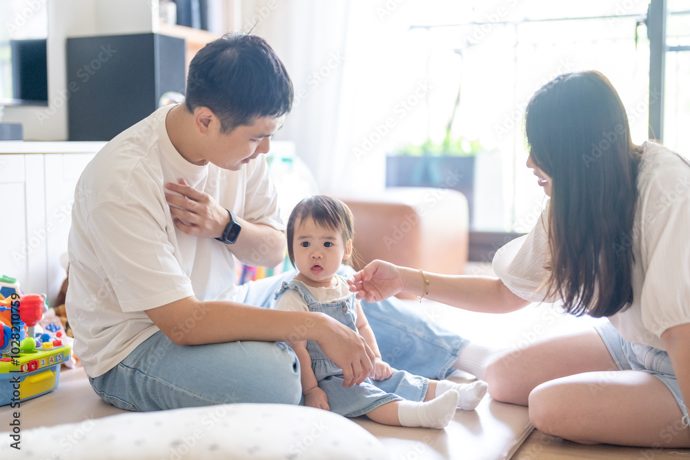 Obraz premium A 1 year old Taiwanese girl spending time playing happily with her parents, a man and woman in their 20s, in a room of a high rise apartment in Taichung City, Taiwan.