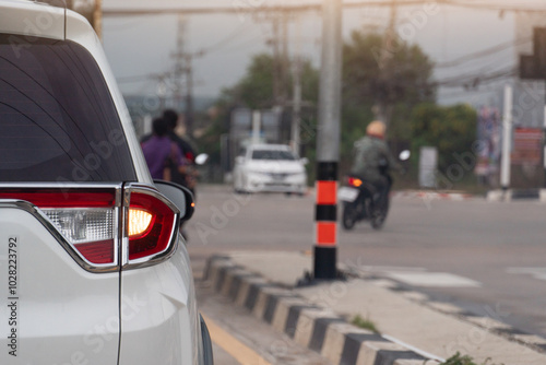 Busy intersection with a white car in the foreground with turn light signal for u-turn. Motorcycle is visible turning right at the intersection. While another vehicle is waiting in the distance.  photo