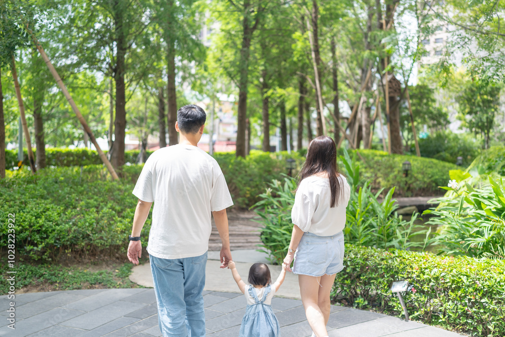 A 1 year old Taiwanese girl walking hand in hand with her parents, a man and woman in their 20s, on a hot sunny day in the streets of Taichung City, Taiwan, in September. A 1 year old Taiwanese girl walking hand in hand with her parents, a man and woman in their 20s, on a hot sunny day in the streets of Taichung City, Taiwan, in September.