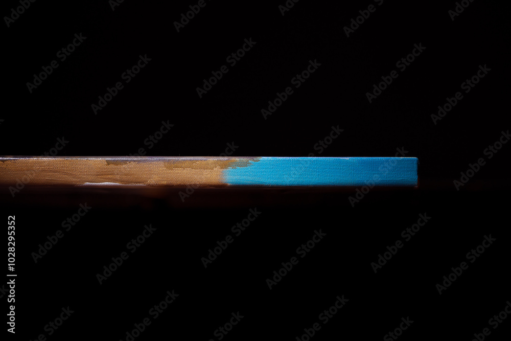 Side view of the canvas stretched on a stretcher. The concept of the modern school of art. Dark brown background. The work of art lies on a wooden table. Side view of the canvas stretched on a stretcher. The concept of the modern school of art. Dark brown background. The work of art lies on a wooden table.