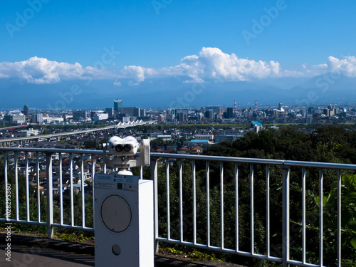 呉羽山展望台の望遠鏡と眼下に広がる富山市市街地と北アルプスの白い雲浮かぶ