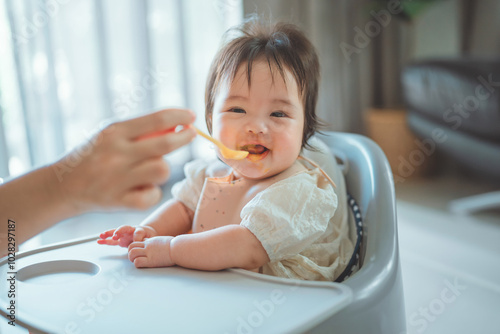 Closeup of Happy asian baby girl eating first food pumpkin from spoon with mom at home