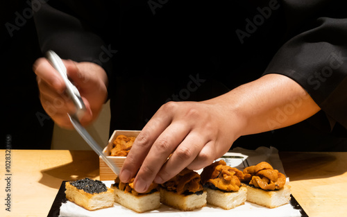 Close up of Japanese chef carefully plating sea urchin on toasted bread set showcasing fine dining preparation with precision and detail on a counter in the restaurant