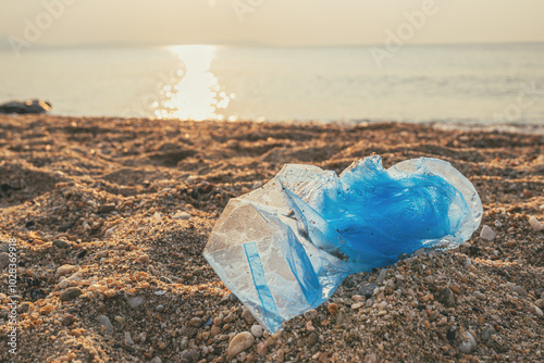 Fototapeta Naklejka Na Ścianę i Meble -  Blue plastic bag at sandy beach in summer sunrise
