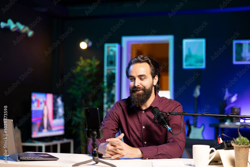 Media star hosting online show in neon lit studio, shooting vlog using mobile phone. Man presenting informations during streaming service broadcast filmed cellphone on tripod