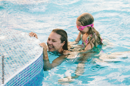 Girl sitting on mother's back swimming in pool photo