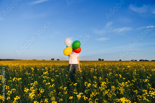 Young woman hiding face with multi colored balloons at rapeseed field under sky photo