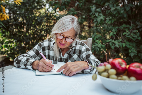 Картината върху платно Beautiful older woman is sitting in the garden and writing in her diary