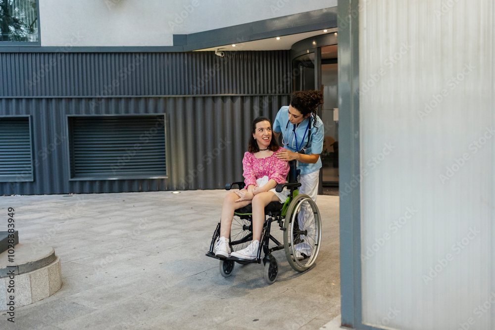Nurse walking with woman sitting on wheelchair at hospital lobby Nurse walking with woman sitting on wheelchair at hospital lobby