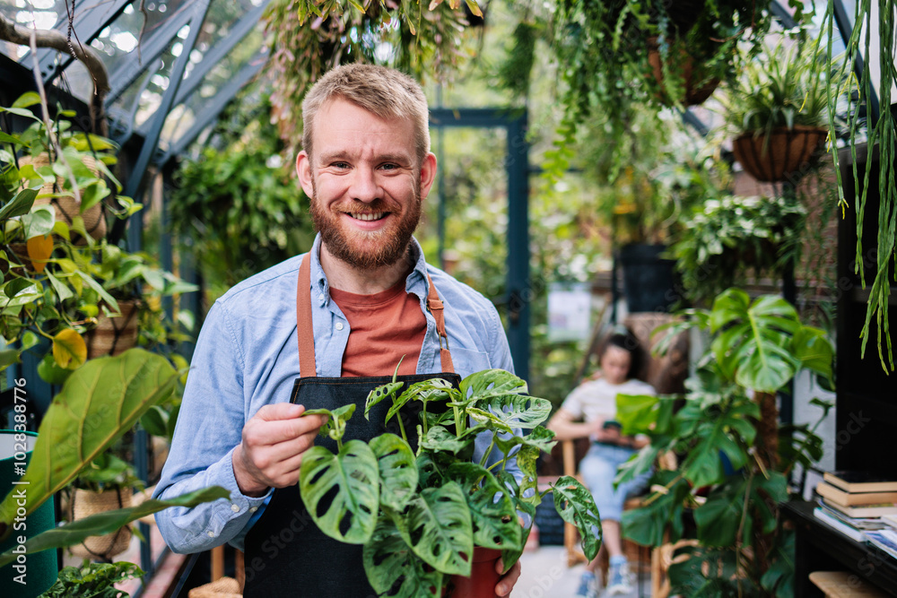 Smiling greenhouse owner holding sapling at garden centre Smiling greenhouse owner holding sapling at garden centre