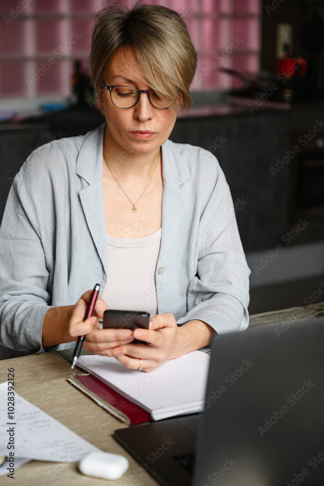 Blond businesswoman with eyeglasses using mobile phone at home Blond businesswoman with eyeglasses using mobile phone at home