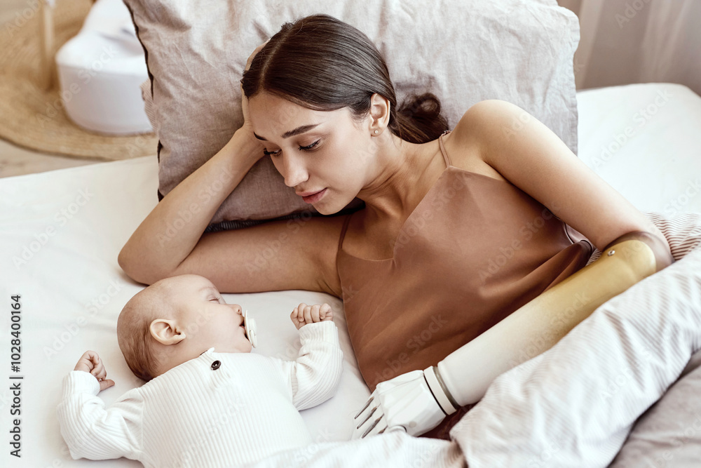 Young woman with amputated arm lying beside sleeping baby boy on bed at home Young woman with amputated arm lying beside sleeping baby boy on bed at home