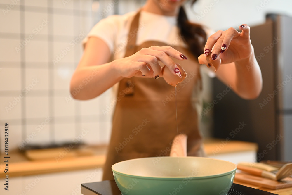 © Prathankarnpap - Young woman cracking an egg into frying pan in a modern kitchen © Prathankarnpap - Young woman cracking an egg into frying pan in a modern kitchen
