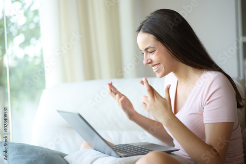 Happy woman crossing fingers expecting checking laptop