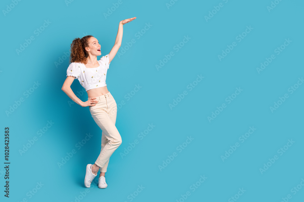 Fototapeta premium Full size photo of pretty young girl show high measure empty space wear trendy white outfit isolated on blue color background