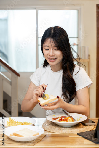 An Asian woman spreads butter on bread for breakfast.
