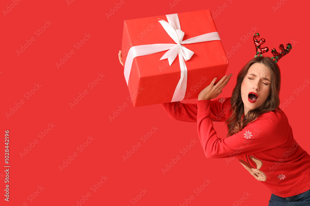 Young woman in reindeer horns with Christmas gift box on red background Young woman in reindeer horns with Christmas gift box on red background