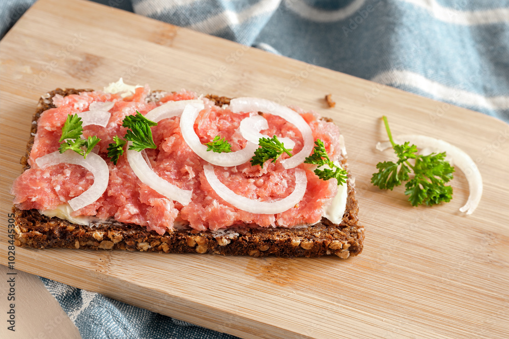 Mett with onions and parsley on a slice of dark wholemeal bread on a kitchen board, German specialty from minced raw pork with low fat seasoned with salt and black pepper, copy space Mett with onions and parsley on a slice of dark wholemeal bread on a kitchen board, German specialty from minced raw pork with low fat seasoned with salt and black pepper, copy space