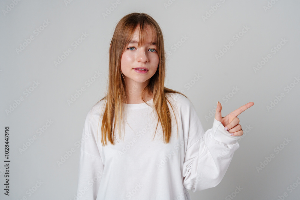 Young girl happily pointing against a neutral background while wearing a cozy white sweatshirt Young girl happily pointing against a neutral background while wearing a cozy white sweatshirt