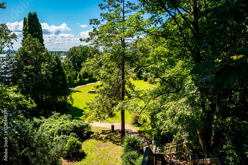 Public park nestled within Hamburg Blankenese, as a wooden staircase descends into the Römischer Garten surrounded by tall trees, vibrant foliage and a landscape ideal for nature walks and relaxation. photo