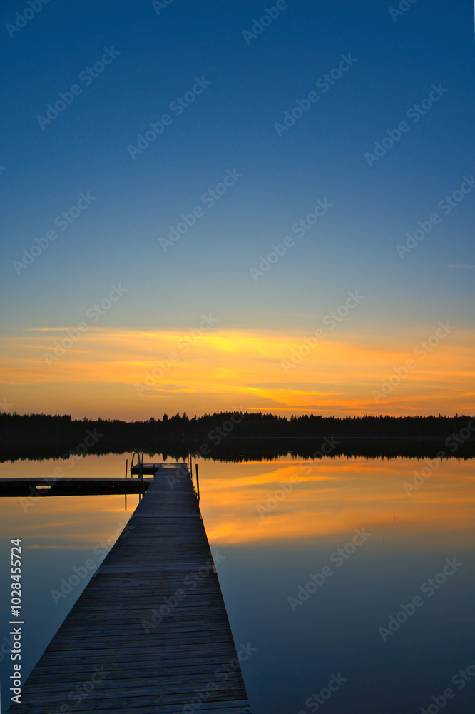 Obraz premium Wooden jetty at sunset on a Swedish lake. The colors are reflected in the water