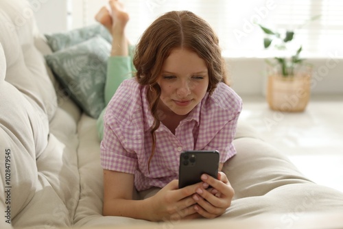 Beautiful teenage girl using smartphone on sofa at home photo