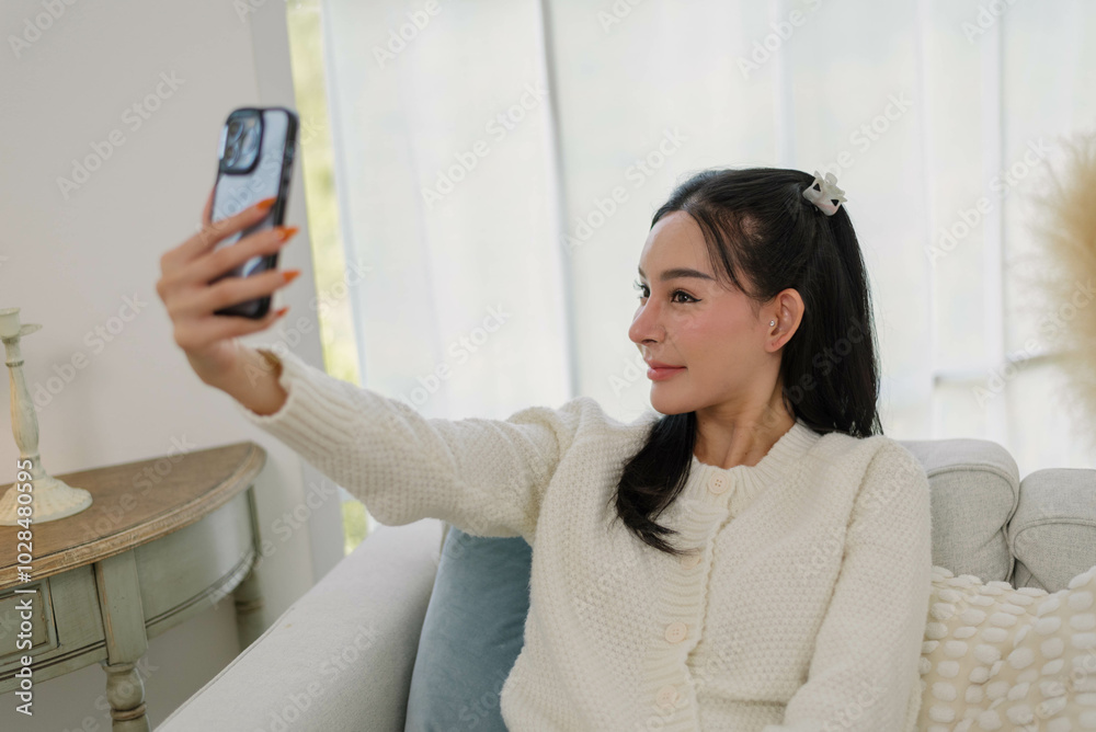Asian woman taking selfie in cozy living Room, young female enjoys a relaxed moment taking photo with her smartphone in a stylishly decorated living room. Lifestyle and daily activities. Asian woman taking selfie in cozy living Room, young female enjoys a relaxed moment taking photo with her smartphone in a stylishly decorated living room. Lifestyle and daily activities.