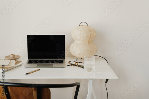 Functional workspace with modern laptop and notebooks on white desk with artistic paper lamp photo