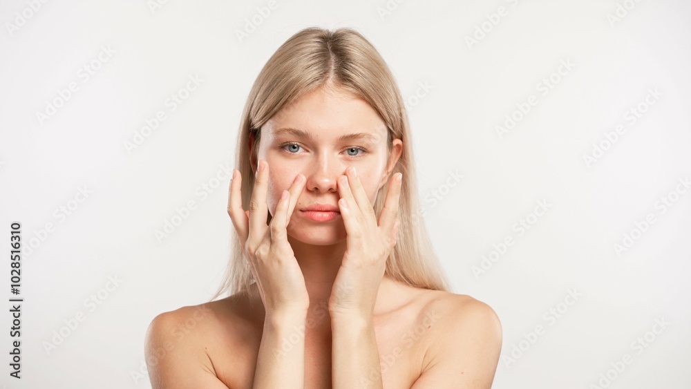 Young blonde woman posing at camera touching smooth face skin with fingers, isolated on white studio background. Beauty skin care concept Young blonde woman posing at camera touching smooth face skin with fingers, isolated on white studio background. Beauty skin care concept