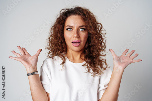 Surprised woman expressing strong emotions with wide eyes and raised hands, studio setting