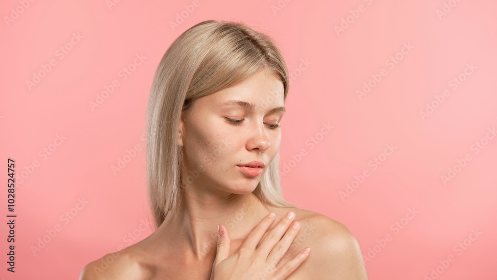 Young blonde woman posing at camera, touches neck and collarbone smooth skin, isolated on pink studio background. Beauty skin care concept Young blonde woman posing at camera, touches neck and collarbone smooth skin, isolated on pink studio background. Beauty skin care concept