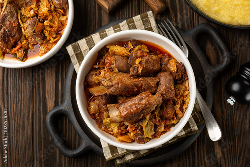 Top view of cassoeula is a typical winter dish popular in western Lombardy, Milanese, North Italian dish. Main ingredients are Savoy cabbage, pork ribs, italian sausage. Polenta. Dark wooden table.. photo