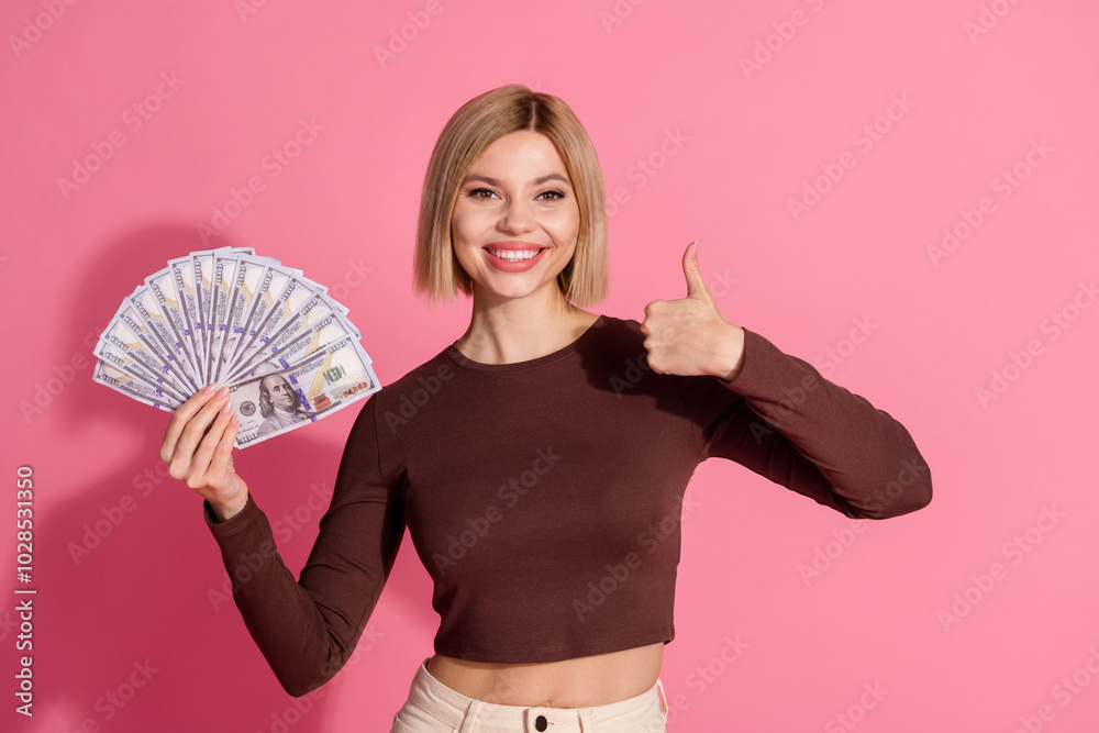 Photo of cheerful adorable girl wear stylish brown clothes hold cash thumb up isolated on pink color background Photo of cheerful adorable girl wear stylish brown clothes hold cash thumb up isolated on pink color background