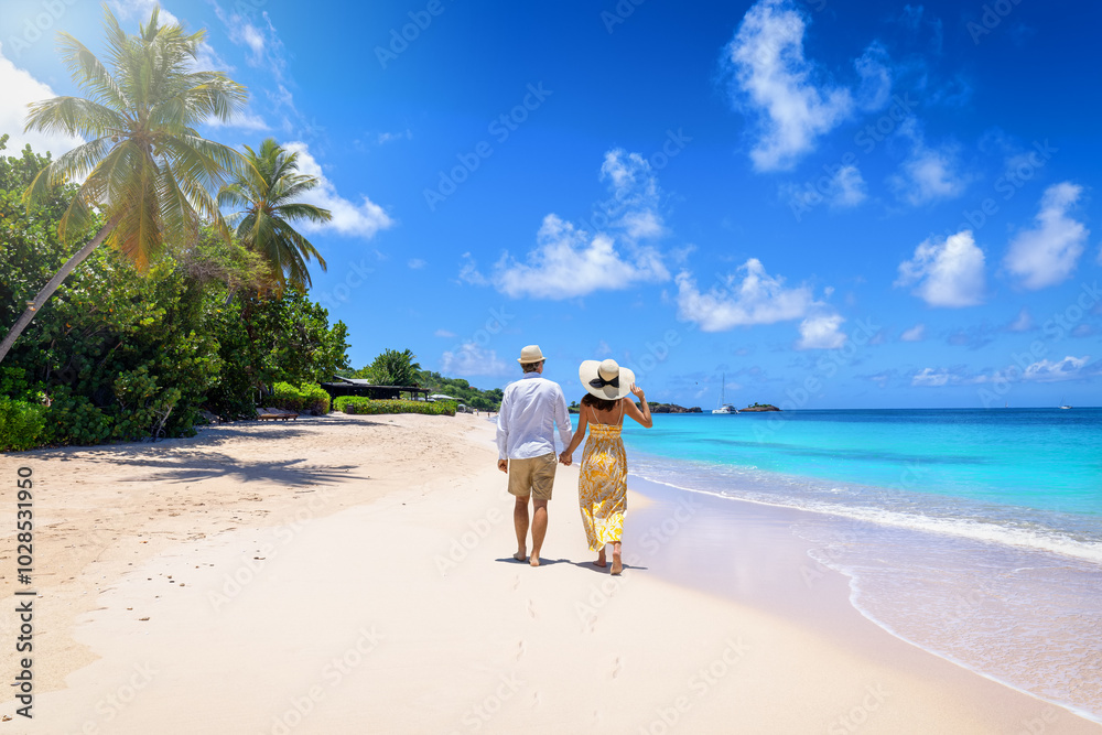 A holiday couple with sunhats walks down the tropical Turners beach with turquoise sea in the Caribbean, Antigua island