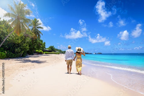 Obraz na płótnie A holiday couple with sunhats walks down the tropical Turners beach with turquoise sea in the Caribbean, Antigua island w salonie