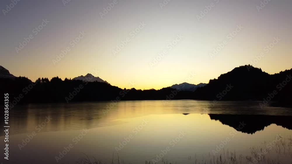 Silhouetted mountain reflection in a calm lake at sunset with clear sky Silhouetted mountain reflection in a calm lake at sunset with clear sky