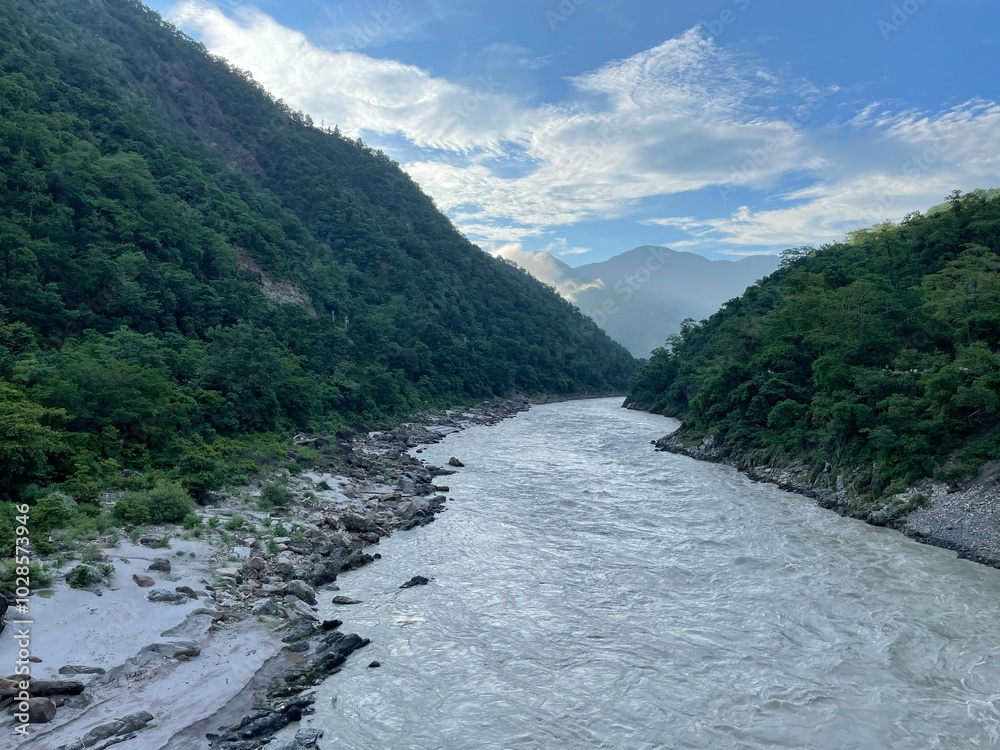 River flowing between lush green mountains under a blue sky. River flowing between lush green mountains under a blue sky.