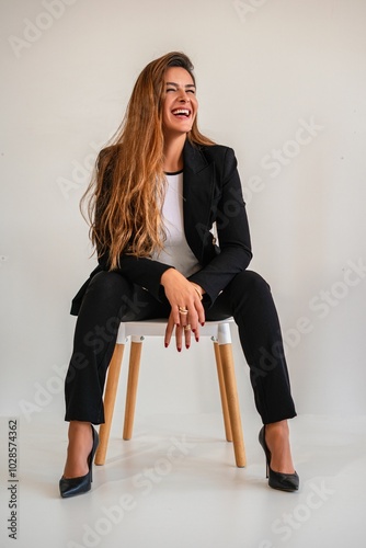 Young woman in a black suit laughing joyfully while sitting. photo