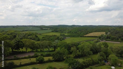 Aerial view of lush green countryside with rolling hills and farmland under a partly cloudy sky.