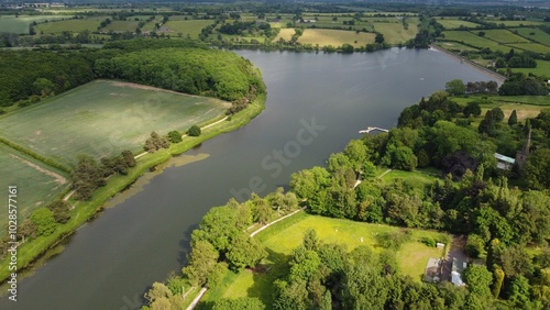 Aerial view of a serene river surrounded by lush green fields and trees on a sunny day.