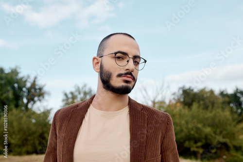 A fashionable man stands confidently in a sunlit field, showcasing autumn style amidst nature's beauty.