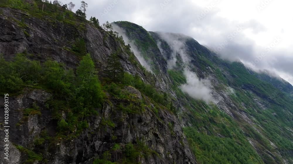 mountain with greenery on its rocky surface, under cloudy sky with low clouds, in Norway mountain with greenery on its rocky surface, under cloudy sky with low clouds, in Norway